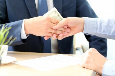 Biznesmeni wykonują gest porozumienia, jeden z nich trzyma plik banknotów.