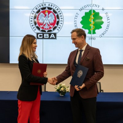Szef CBA oraz Rektor Uniwersytetu Medycznego wymienijają uścisk dłoni, w tle logo CBA oraz Uniwerystetu.