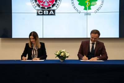 Dwie osoby siedzą przy stole konferencyjnym i podpisują dokumenty.