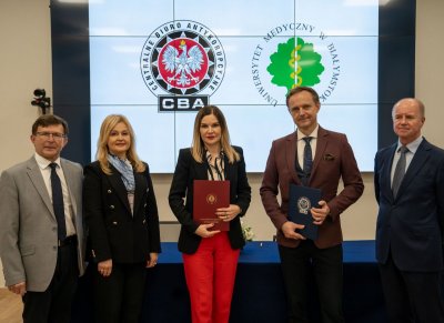 Pięć osób stojących w sali konferencyjnej, w tle logo CBA i Uniwersytetu