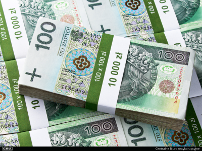 Plik banknotów stu złotowych. W tle więcej banknotów.