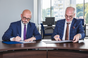 Two men siitting at the desk and signing the kletter about cooperation