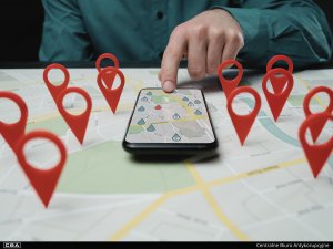 A person pointing to a location on a smartphone map, urrounded by physical map pins.