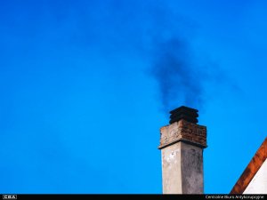 A chimney emitting dark smoke against a blue sky.