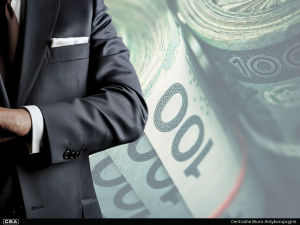 A man in a suit standing, polish banknotes in the background.